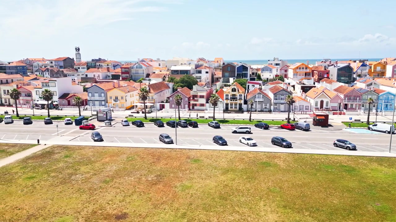 Drone che esegue una panoramica a sinistra su case colorate a strisce e strada costiera ad Aveiro, Portogallo, mostrando architettura marittima, veicoli e dintorni della città