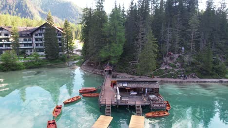 Backwards-aerial-reveals-docked-wooden-boats-reflecting-on-Lago-Di-Braies