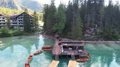 backwards aerial reveals docked wooden boats reflecting on lago di braies