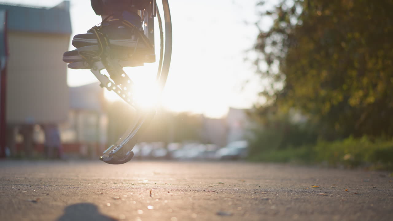 금속 스프링 디자인을 가진 현대적인 인공 팔다리가 밝은 빛 아래 야외 환경에서 점프하는 클로즈업. 배경에는 에너지와 활동을 암시하는 흐릿한 녹색 공원이 있습니다.