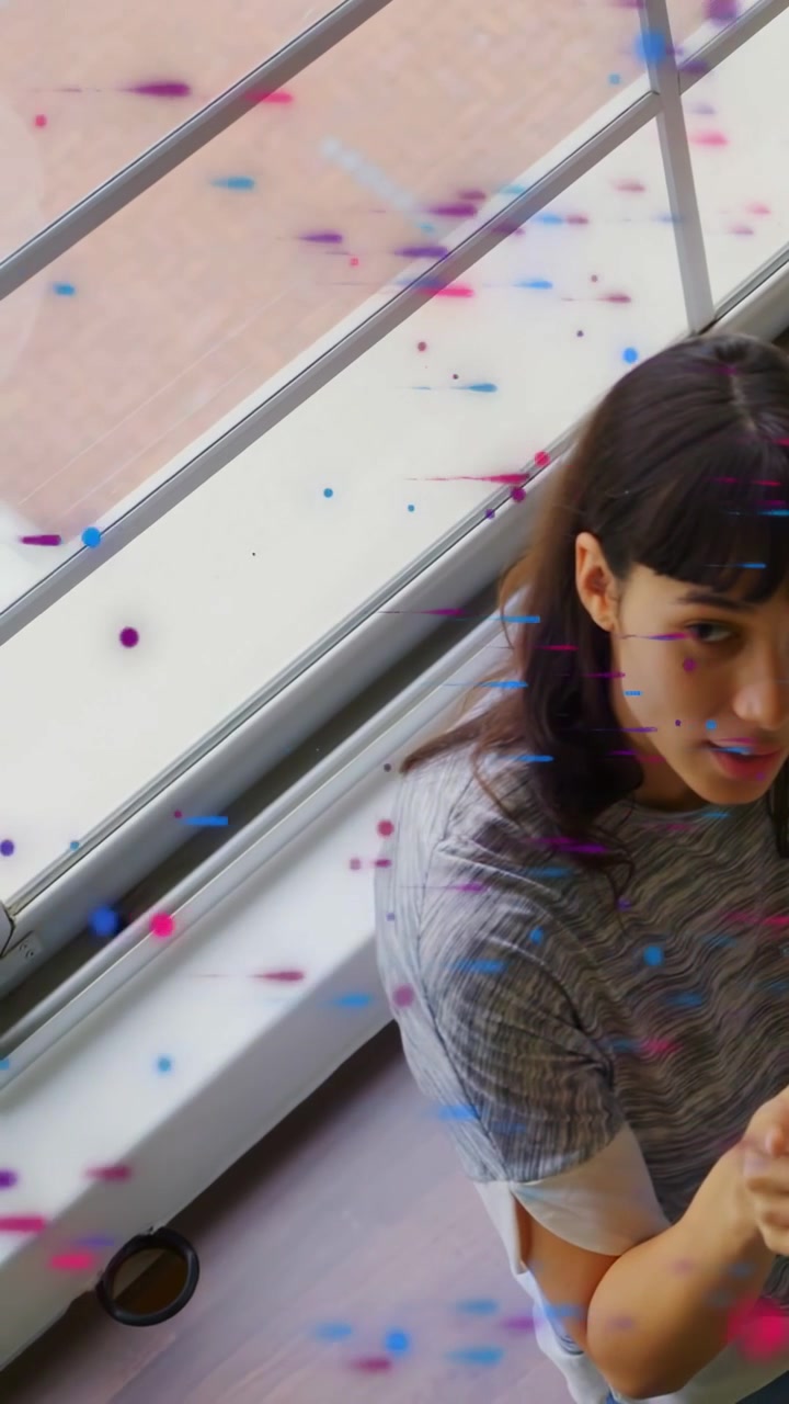 Vertical video: Woman pointing at camera making confetti while turning away near window for design