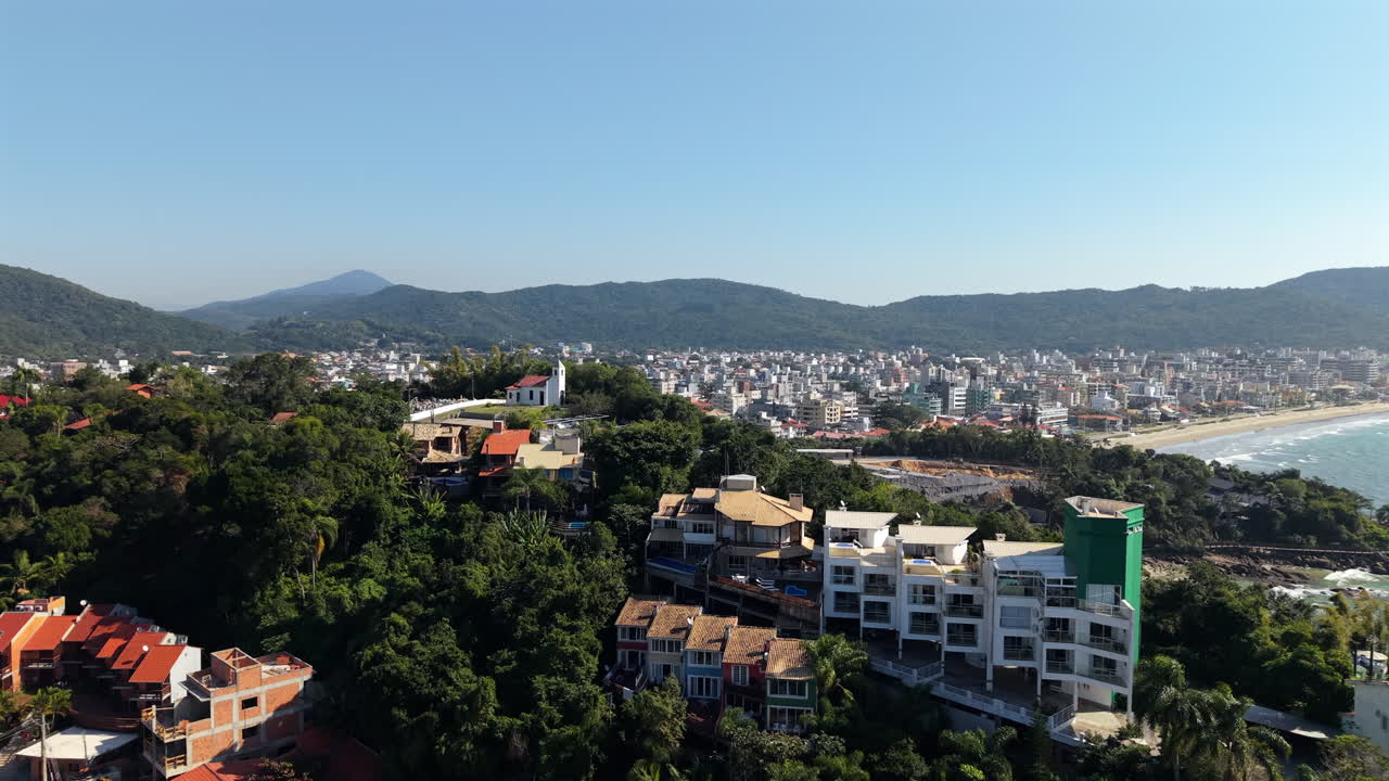 Rising aerial reveals Bombas district of Bombinhas, SC, with hillside homes, beach and city