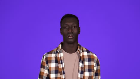 sick young african man coughing hard and hitting himself the chest isolated on blue background. wearing plaid shirt