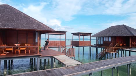 Un-Turista-Masculino-Saliendo-De-Una-Lujosa-Villa-Privada-Sobre-El-Agua-Con-Equipaje-En-Un-Resort-Tropical-Durante-El-Día