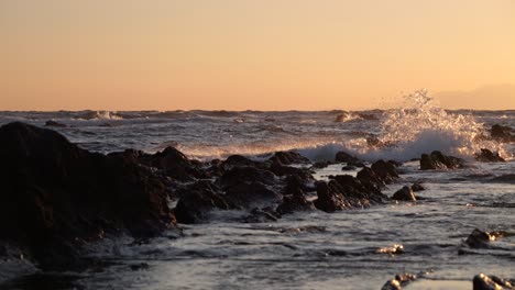 Low-angle-cinematic-slow-motion-shot-of-silhouette-rocks-in-ocean-during-sunset