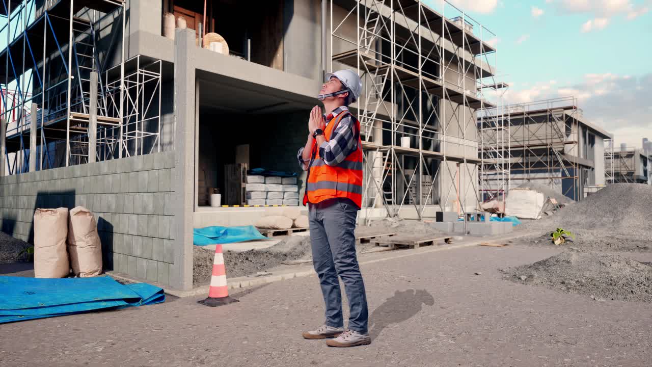 Full Body Side View Of Asian Male Engineer With Safety Helmet Pray For Something While Standing At Building & Construction Site in Progress to New House