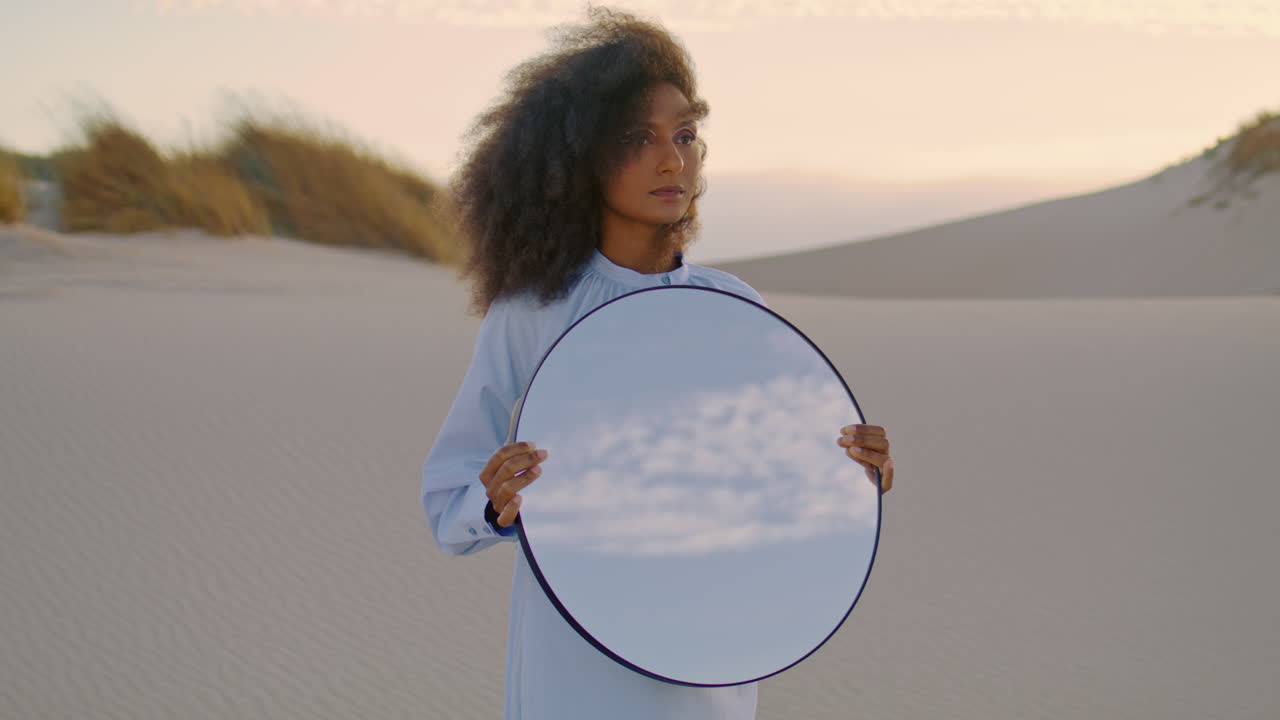 Primo piano di donna che tiene uno specchio nel deserto di sabbia in estate. Ragazza in piedi nella natura selvaggia.