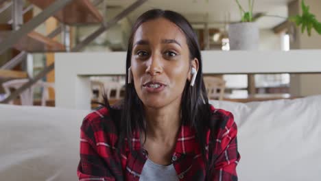 Mixed-race-woman-on-couch-at-home-using-laptop-having-video-chat