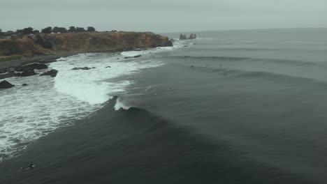 Aerial-Shot-of-surfers-catching-a-wave-on-a-cloudy-day-in-Punta-de-Lobos-4K