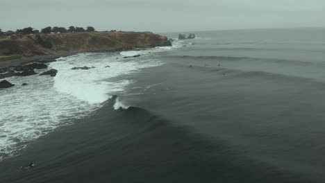 aerial shot of surfers catching a wave on a cloudy day in punta de lobos-4k