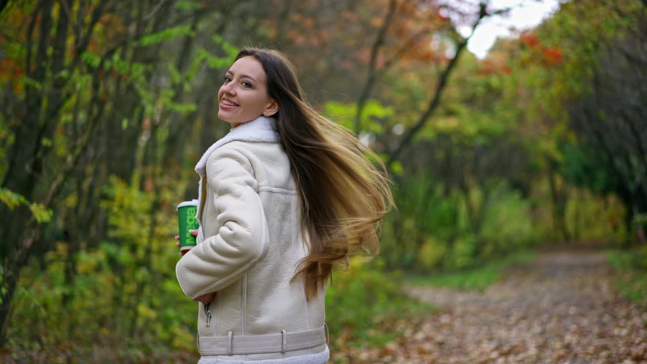 Following the brunette long-haired lady walking by the park. Woman turns around, walks backwards and then turns again, camera view on her feet.
