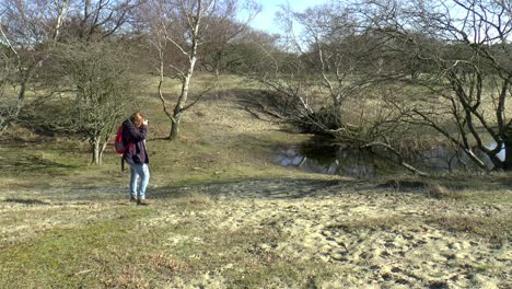 woman with red backpack takes a picture with her camera of a pool in the dutch dune landscape