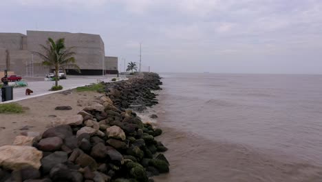 Aerial-Veracruz-shore-forward-flies-by-modern-building-rock-shore-coastline-day