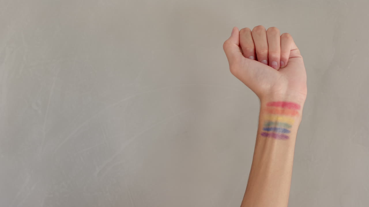 Raising fist, person showing rainbow pride flag painted on wrist