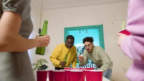 happy multiethnic young friends playing beer pong at home