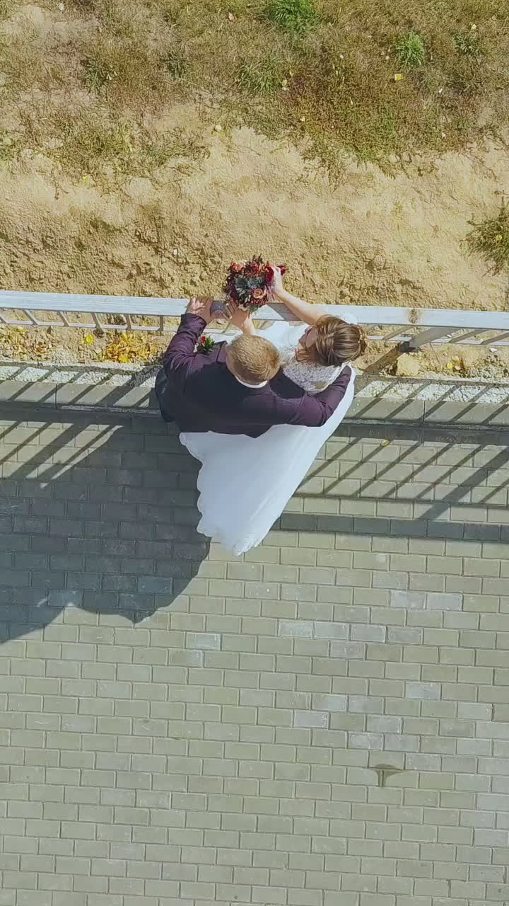 lovely newly wedded couple kisses near asphalt ground railing along lawn on sunny autumn day upper view
