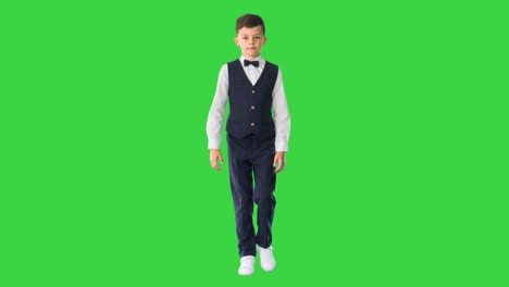 little boy in a waistcoat and a bow tie walking looking straight ahead on a green screen, chroma key