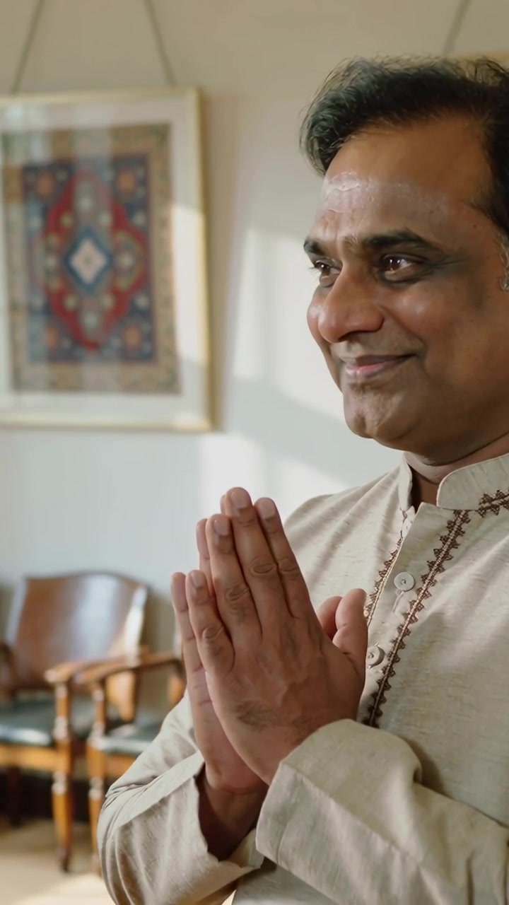 Vertical video: Spotting guest, Indian man in kurta greeting Namaste in well-lit room, tapestry