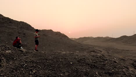 aerial shot of the mountains of shawka, fujairah during orange sunset with teenager pilot