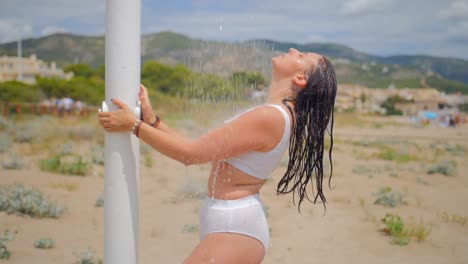 side view of a sexy woman in white swimwear taking a shower outdoor at the beach in summer. slow motion