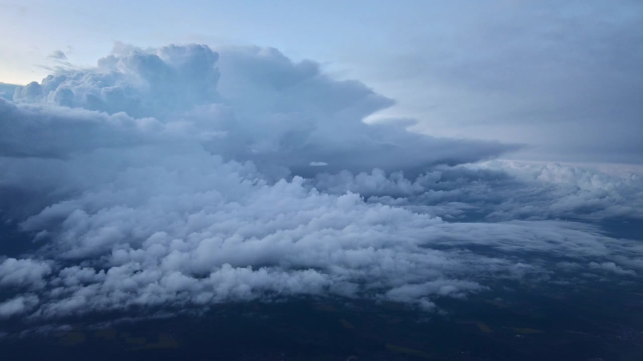 View from a plane of towering storm clouds and a low cloud layer above a dark landscape at dusk