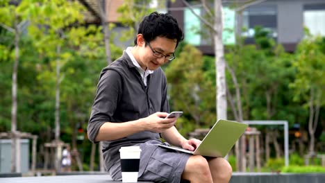 casual asian man using laptop and celebrating with his job in the park