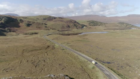 A-yellow-campervan-drives-along-a-long-scenic-curvy-road-up-through-Scottish-hills-and-mountains