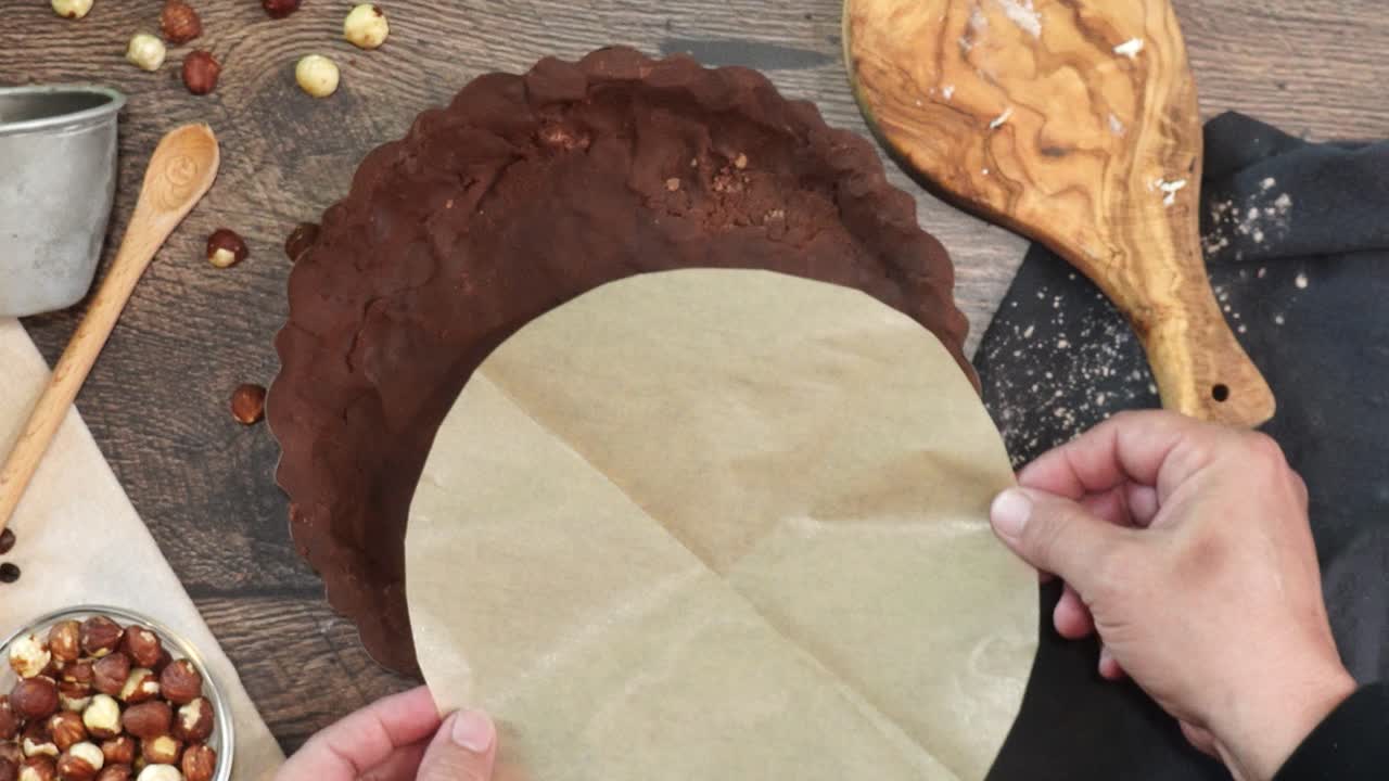 A delicious dessert, Coffee Hazelnut Cream Tart. Made with espresso powder, chocolate crust and loaded with crushed hazelnut. Adding round natural parchment paper to the chocolate crust on a table