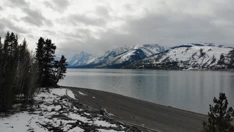 A-low-flying-drone-shot-off-the-coastline-of-Jackson-Lake,-with-the-Grand-Teton-Range-in-the-background,-in-Grand-Teton-National-Park-of-Northwestern-Wyoming