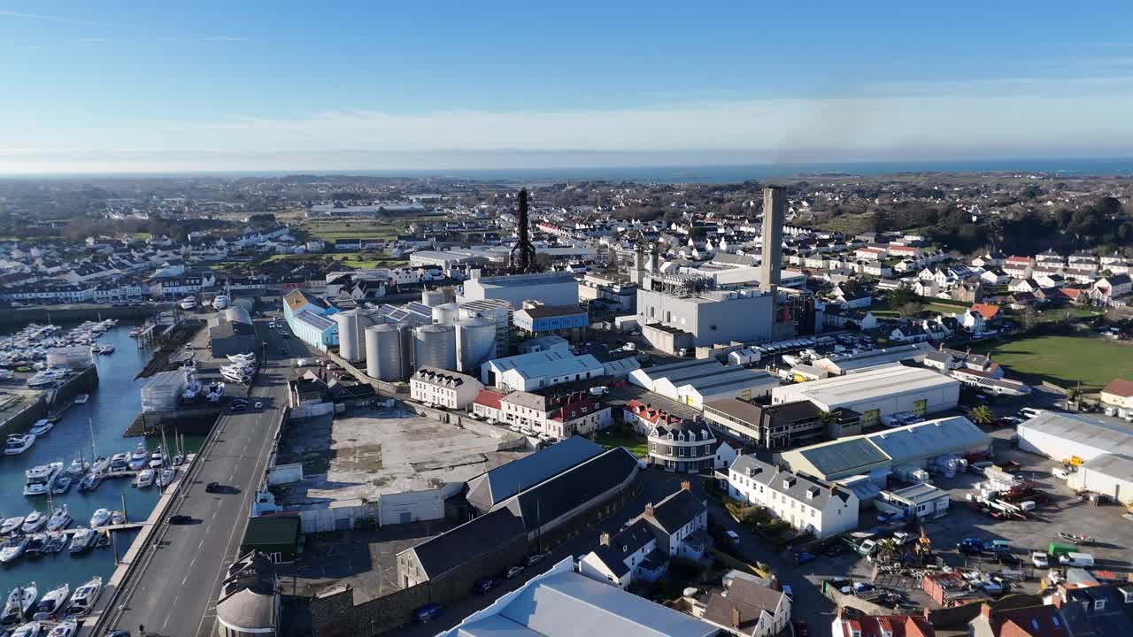 Guernsey drone flight over Industrial zone in St Sampsons pulling back from power station showing harbour and marina in bright late afternoon sunlight with blue sky and full perspective of area