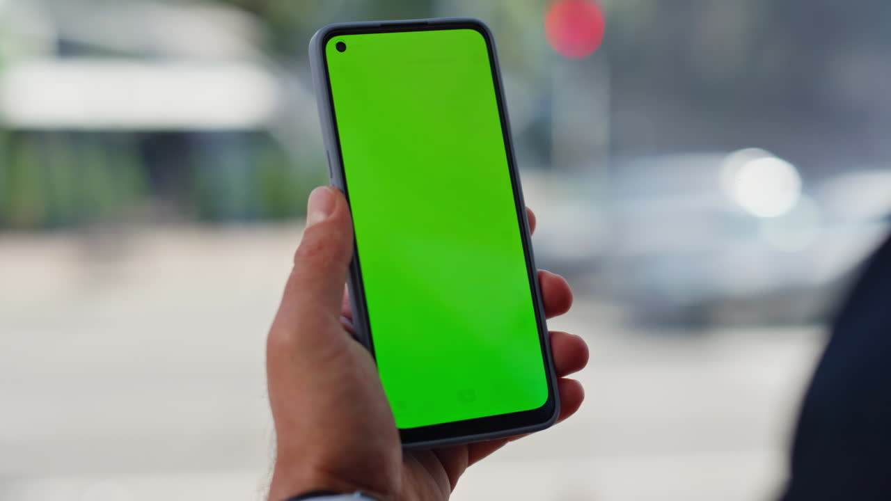Hand tapping smartphone green screen browsing online in city view place closeup