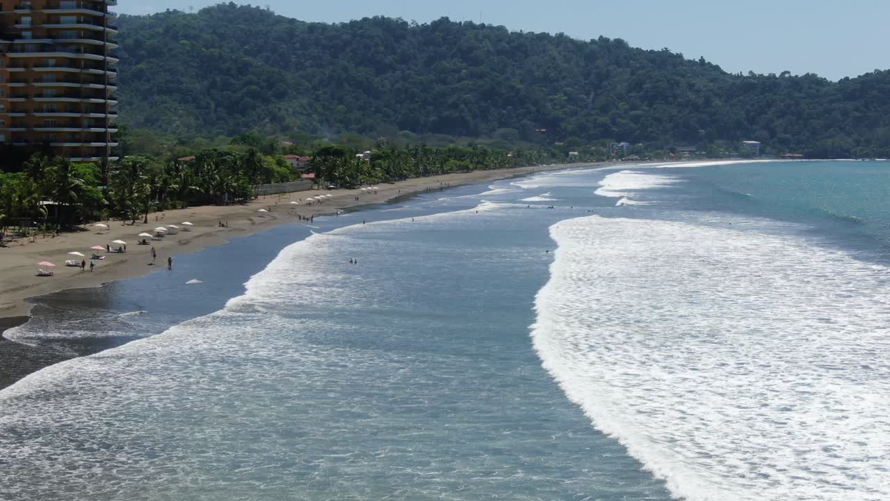 vista de drones de la playa de costa rica que muestra el mar del océano pacífico con olas y surfistas sentados en sus tablas en jaco en un día soleado