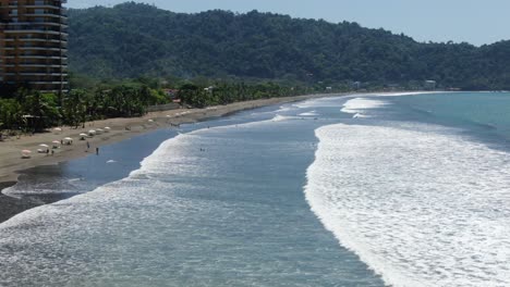 costa rica beach drone view showing the pacific ocean sea with waves and surfers sitting on their boards in jaco on a sunny day