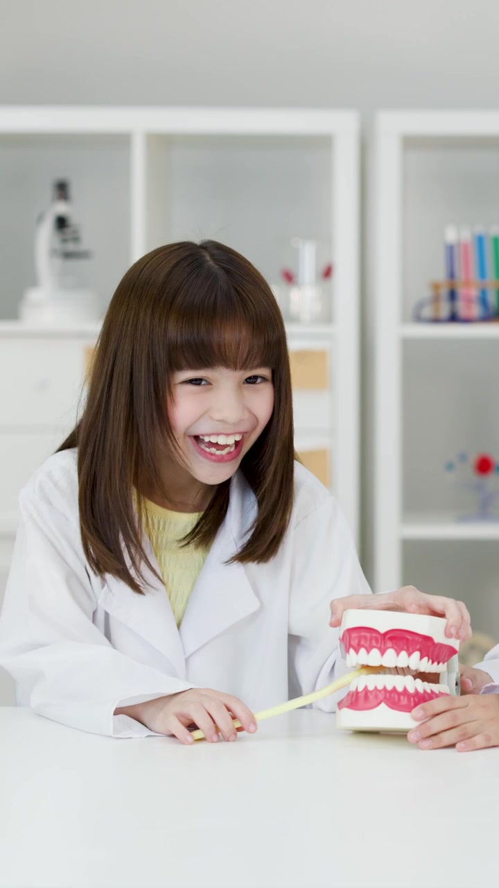Smiling young student uses a toothbrush on a dental model in a bright science classroom.