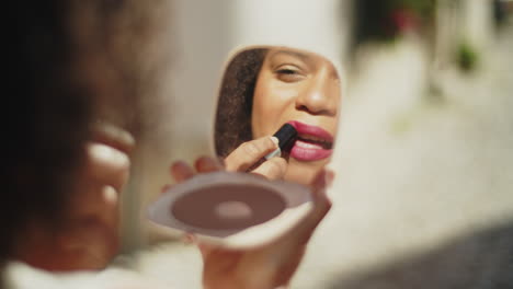 reflexo de uma mulher afro-americana sorridente olhando no espelho e aplicando batom