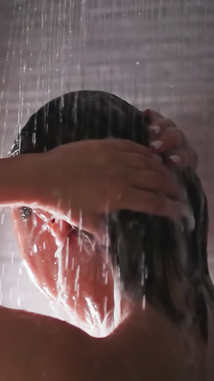 Woman washes hair under shower sprays closeup. Bare lady removes foam from head with water flow in bathroom. Woman enjoys body washing at home