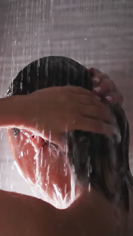 woman washes hair under shower sprays closeup. bare lady removes foam from head with water flow in bathroom. woman enjoys body washing at home