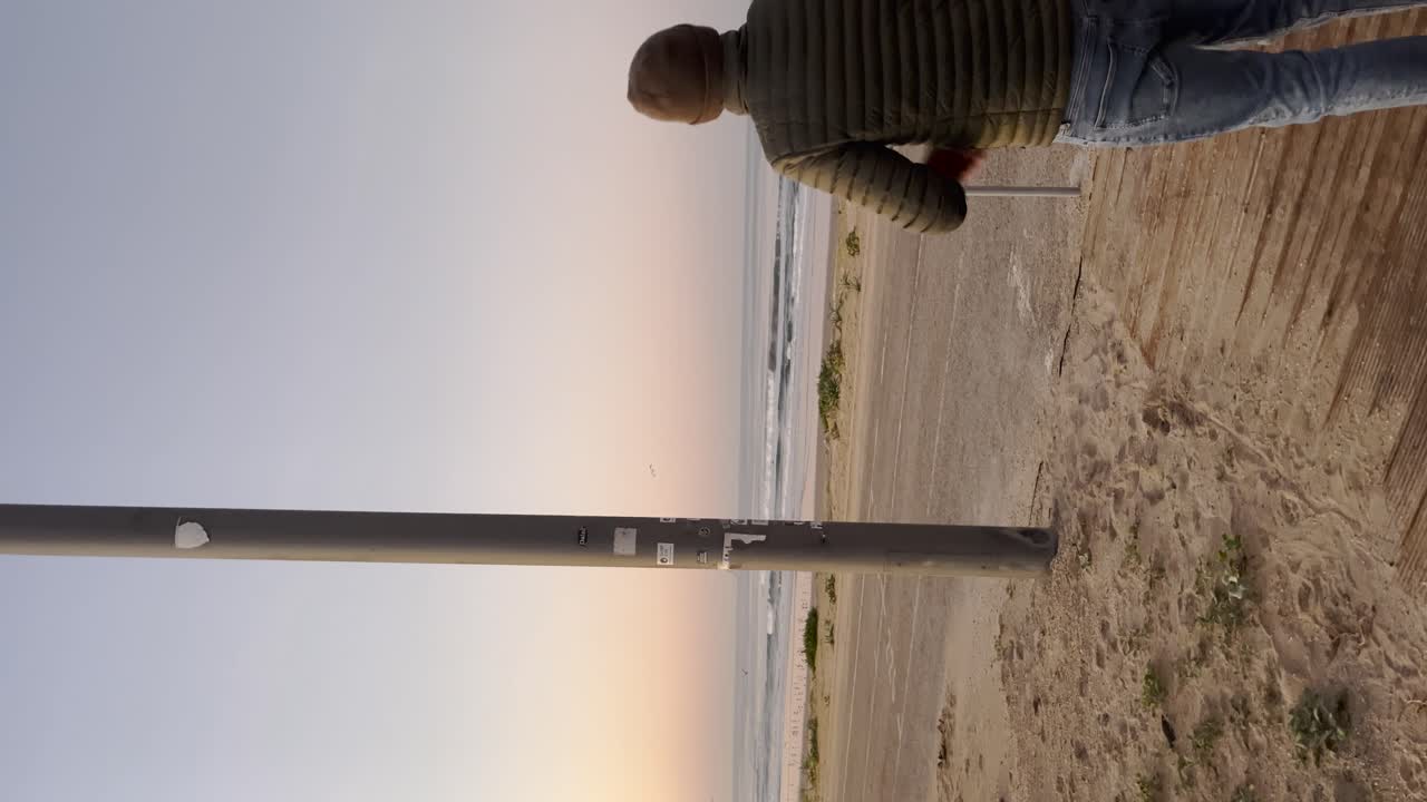 video vertical de la costa portuguesa durante la puesta de sol, con una persona observando el entorno tranquilo de la playa. una escena serena y contemplativa que mezcla la presencia humana con la belleza de la naturaleza.