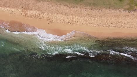 Turquoise-ocean-water-foaming-at-the-shore,-washing-the-golden-sand-of-the-beach-with-footprints,-Idyllic-summer-vacation-in-Hawaii