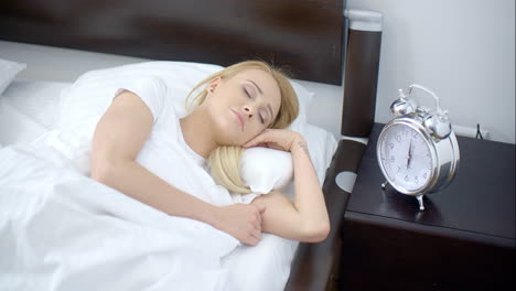 pretty sleeping woman with alarm clock next to her