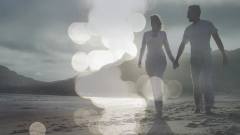 Composite-video-of-spots-of-light-against-caucasian-couple-walking-on-the-beach