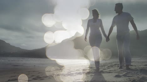 composite video of spots of light against caucasian couple walking on the beach