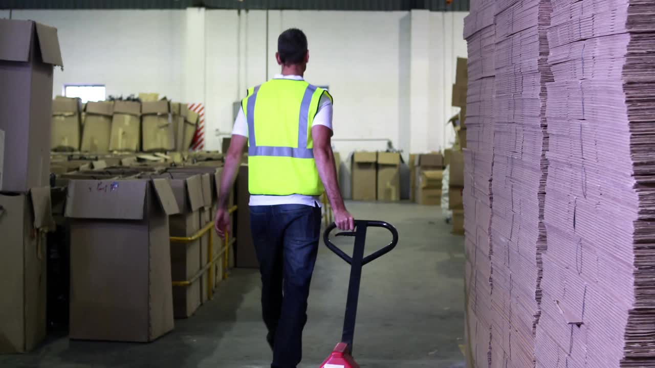 Warehouse operator gripping and pulling red pallet jack aisle scanning item codes with blue beam