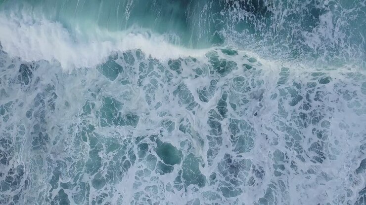 overhead drone shot of sea waves with white foam
