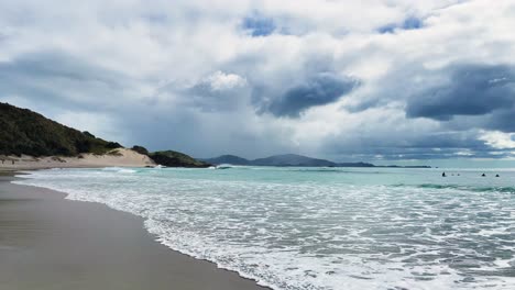 calm waves break at shore on overcast day, wide shot in slow motion