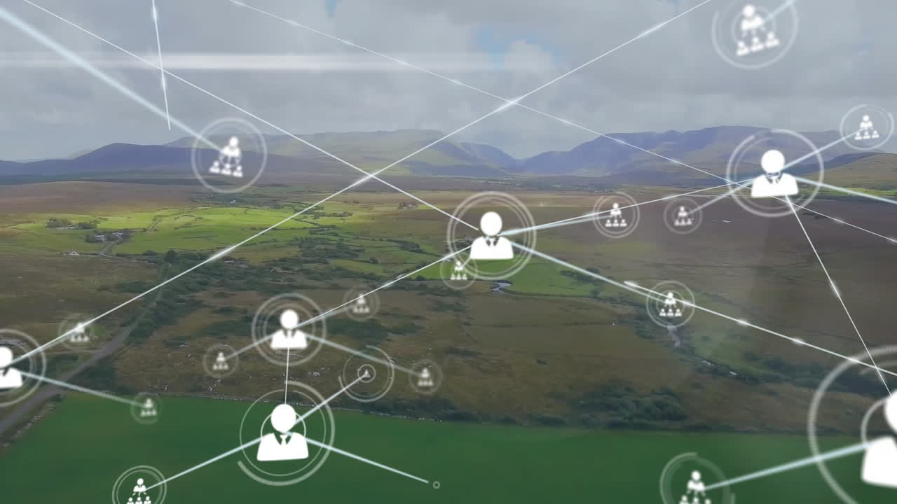 Animation of connected icons over aerial view of green land against mountains and cloudy sky