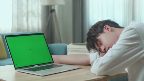 primer plano de un estudiante asiático durmiendo mientras usa una computadora de pantalla verde en casa