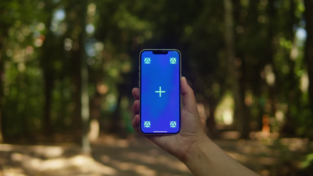 Young woman holding phone chroma key screen in the lovely park close-up. Girl with green screen on smart phone. Nature.