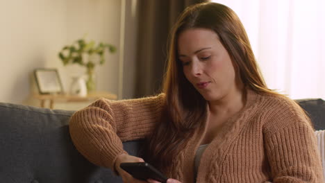 woman sitting on sofa at home using mobile phone to check social media message and scrolling online 18