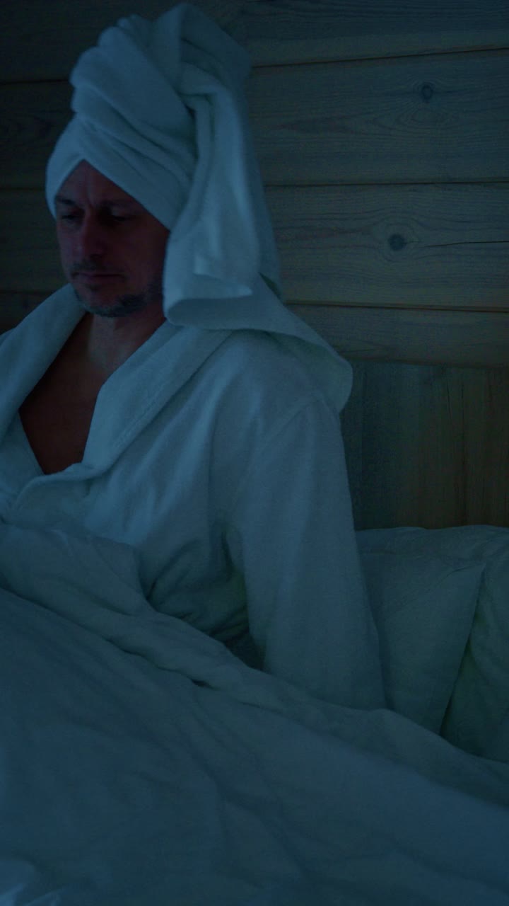 Relaxing evening routine with a man in a bathrobe checking his phone in a cozy bedroom